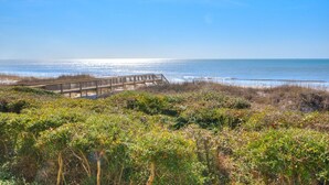 A coastal landscape with a wooden boardwalk leading to the beach, surrounded by dense vegetation. - Oceanfront OIBV 207 in Oak Island, NC: 3 beds, stunning beach views, sleeps 6! (Oak Island)