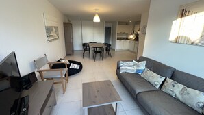 A modern living room with a sofa, coffee table, and chairs. There is a dining table with chairs in the background.