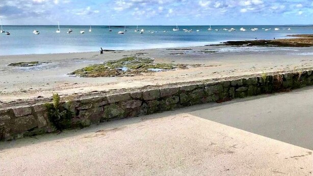 A beach with boats, a stone wall, and a paved walkway.