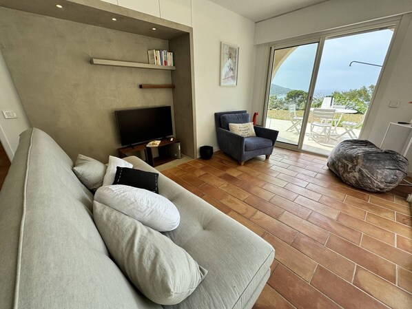 Una sala de estar con un sofá gris, un televisor, una silla y un sillón de pie.