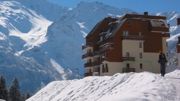 Um edifício de vários andares com varandas, com montanhas cobertas de neve ao fundo.