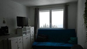 Um quarto pequeno e simples, com uma cama, uma escrivaninha e uma televisão.