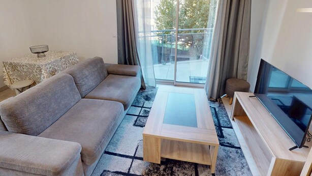Un salon avec un canapé, une table basse, un téléviseur et un balcon agrémenté de rideaux.