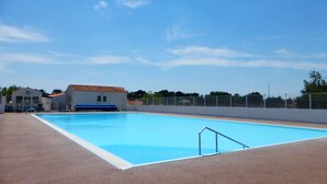 A swimming pool with a clear blue sky, a white building with a red roof, and a fence in the background.