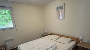 A bedroom with a single bed, a nightstand, a lamp, a heater, and a window with a view of greenery. - Spacious well-equipped chalet with parking in Cauterets (Cauterets)