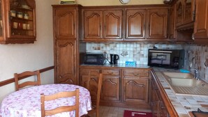 A kitchen with wooden cabinets, a dining table with chairs, a microwave, and a sink. - Charming cottage with garden, WiFi, pets welcome (Thorigné-sur-Dué)