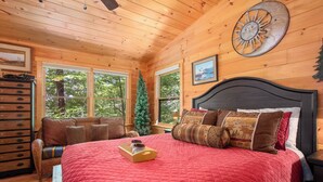Une chambre confortable dans un chalet en bois, avec un grand lit, une commode, une chaise et un sapin de Noël.