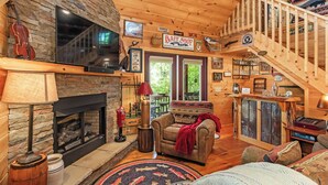 L’intérieur d’un chalet accueillant, avec une cheminée en pierre, un téléviseur, un canapé et un escalier.