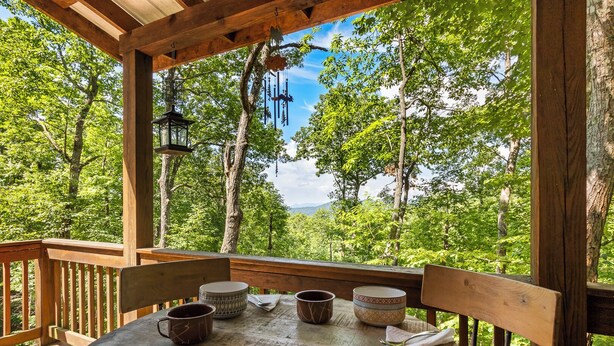 Une terrasse en bois avec une table dressée pour le repas, entourée d’arbres et offrant une vue dégagée sur le paysage.