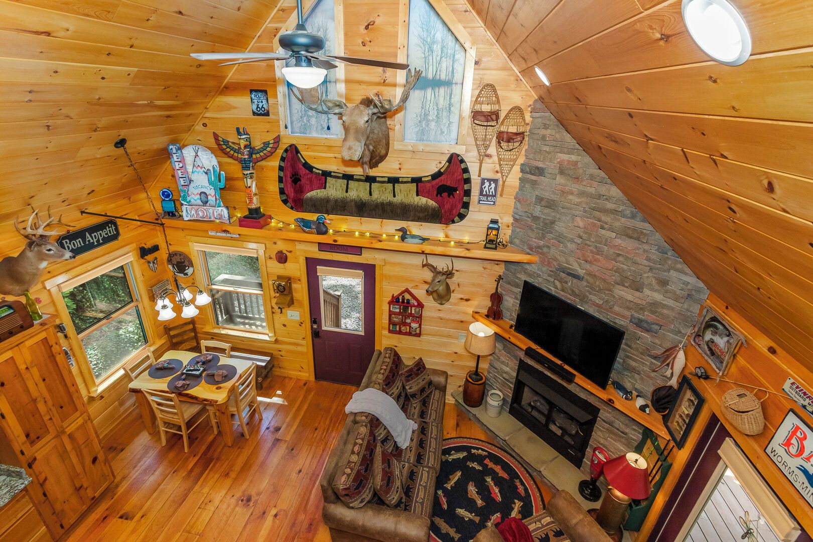 A cozy log cabin with a dining area, a fireplace, and various decorations including animal heads and a sign reading "Bon Appetit".
