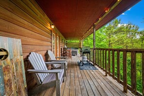Een houten terras met Adirondack stoelen, een barbecue en een tafel.