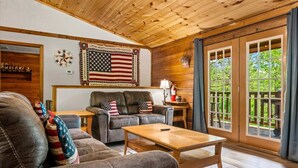 A cozy living room with a leather couch, a wooden coffee table, and a large American flag on the wall. - New! 3BR*Hot Tub*Game Room*Jacuzzi*Near Dollywood* (Sevierville)