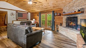 A cozy living room with a fireplace, wooden ceiling, and a large American flag. - New! 3BR*Hot Tub*Game Room*Jacuzzi*Near Dollywood* (Sevierville)