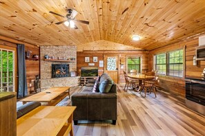 A cabin interior with a fireplace, wooden walls, a dining area, and a television.