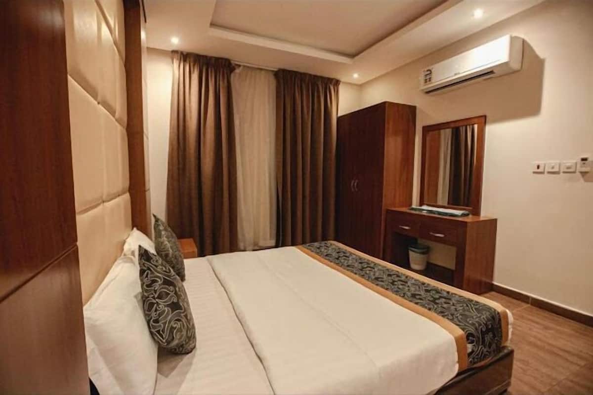 A hotel room with a large bed, a wooden wardrobe, a mirror, and an air conditioning unit.