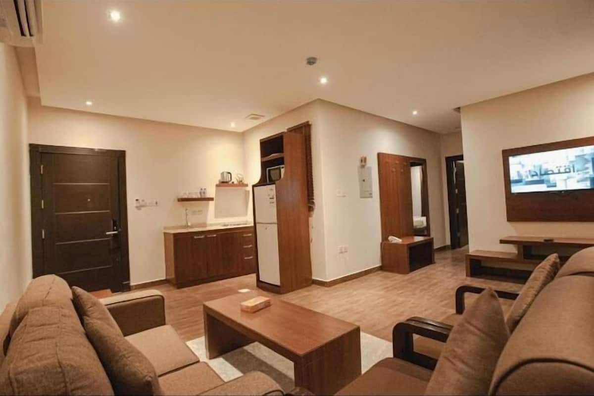 A compact living space with a kitchenette, a sofa, a coffee table, and a flat-screen TV.