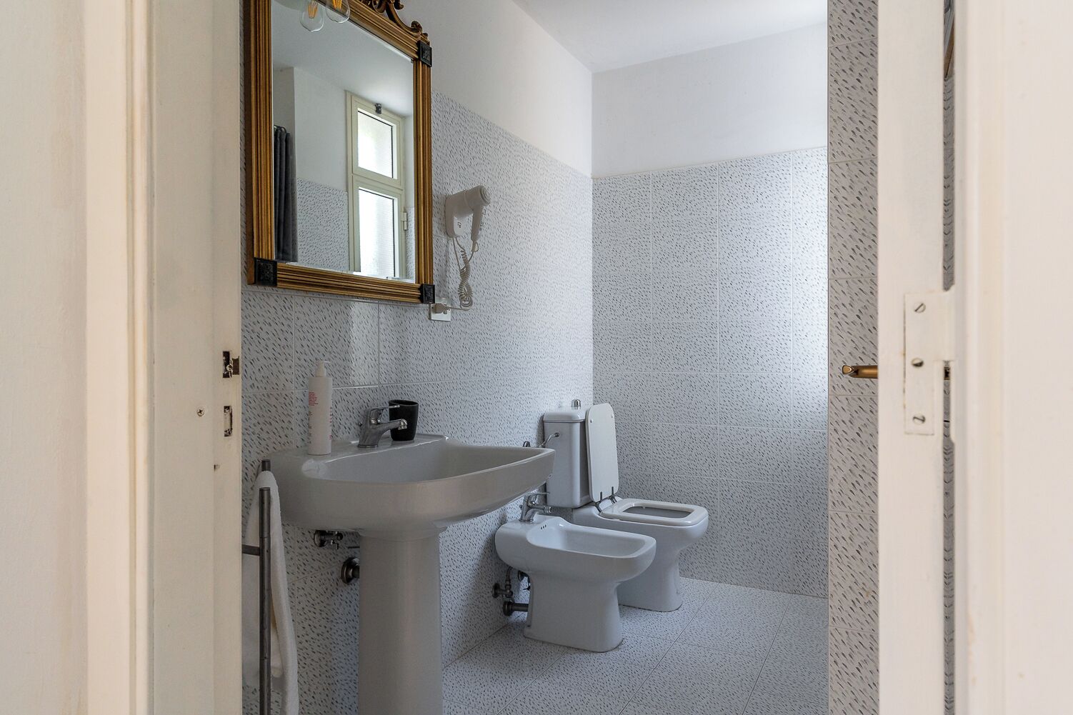 Un baño con lavamanos, dos inodoros y un secador de pelo.
