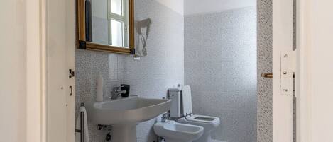 Un baño con lavamanos, dos inodoros y un secador de pelo.