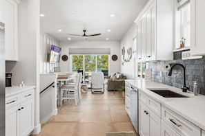 A modern kitchen with white cabinetry, a stone backsplash, and a dining area with a view. - Gulfside Sunset - 2309A   “Anna Maria Island” (Bradenton Beach)