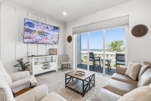 A modern living room with a large TV, a sofa, a coffee table, and a balcony with outdoor furniture. - Gulfside Sunset - 2309A   “Anna Maria Island” (Bradenton Beach)