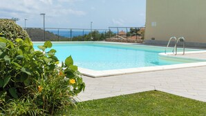 A swimming pool with a clear view of the sea in the background, surrounded by a well-maintained lawn and a building with a balcony. - Perla Abernathy - vacation home by the sea with pool and garden (Boissano)