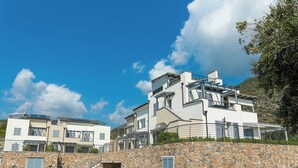 A modern multi-story building with a stone retaining wall, a staircase, and a parking area. - Perla Abernathy - vacation home by the sea with pool and garden (Boissano)