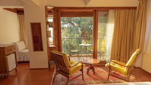 Una stanza con un letto, due poltrone gialle, un tavolino, una libreria e vista su alberi attraverso un'ampia finestra.