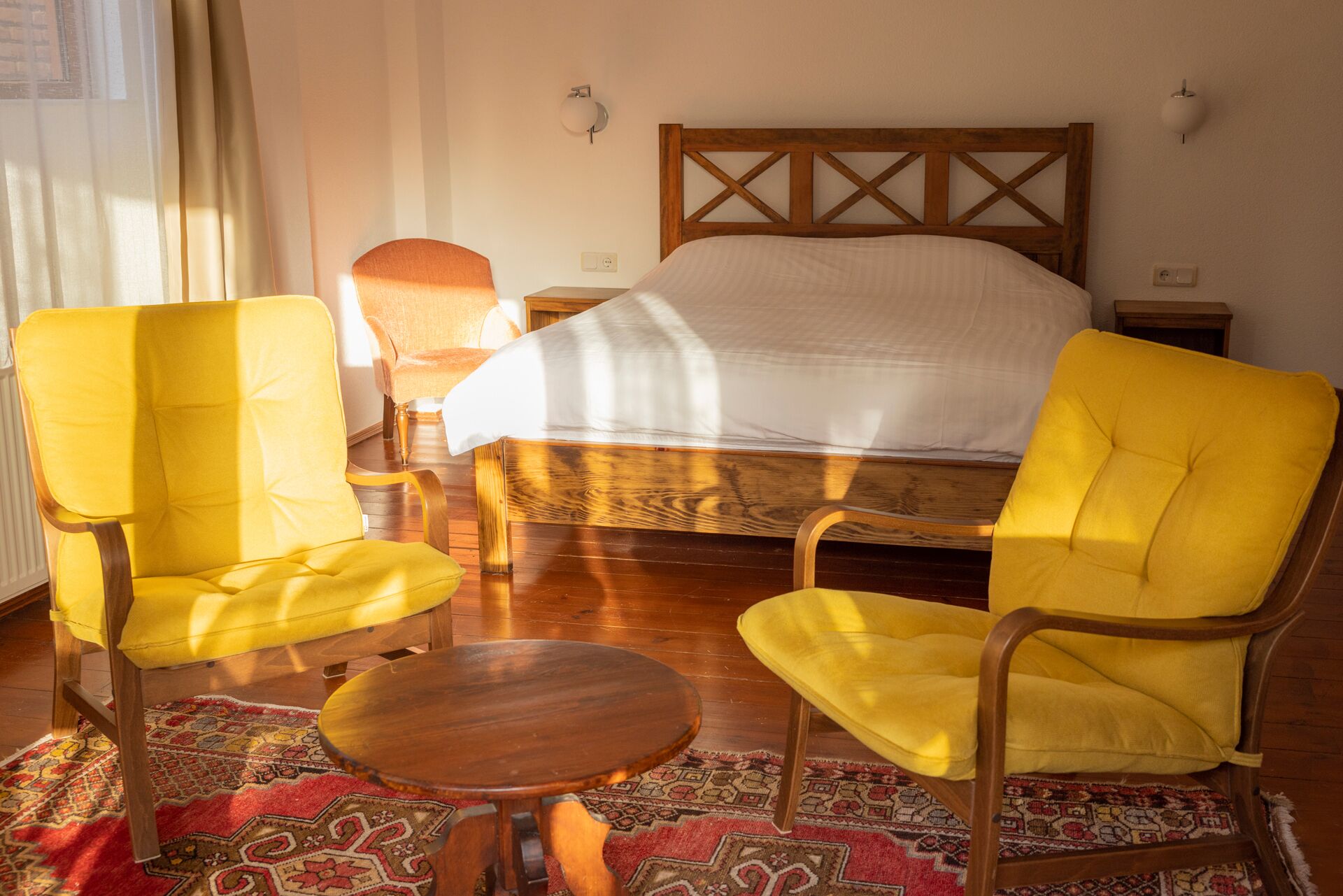 Una stanza con un letto, due poltrone gialle, un tavolino rotondo e tappeti decorati.