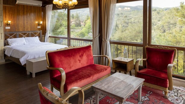 Una camera da letto con un letto, un divano rosso, una sedia di legno, un tavolino e vista sull'esterno.