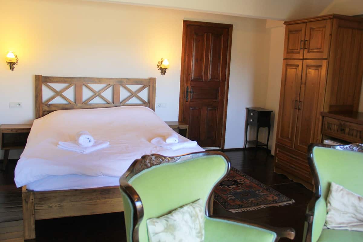 Quarto com cama de madeira, duas arandelas, guarda-roupa de madeira e poltrona verde.