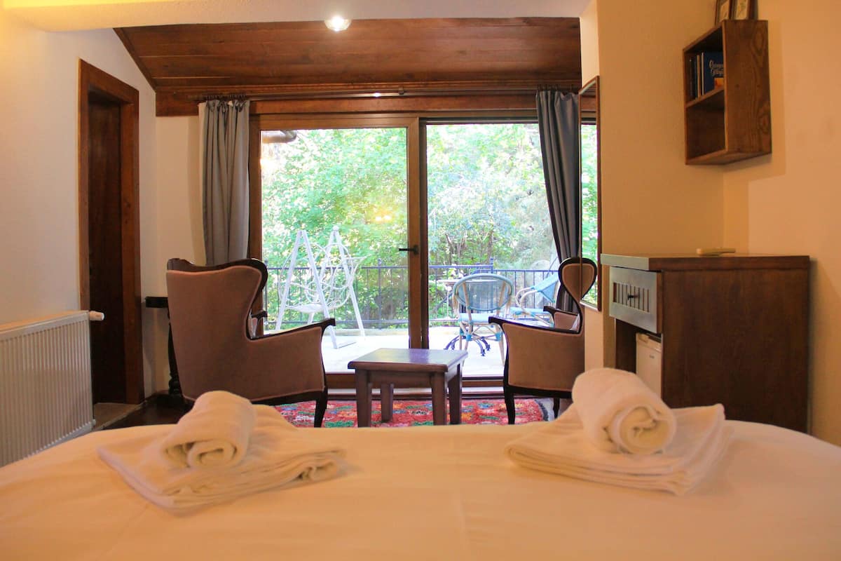 Quarto de hotel com uma cama, duas cadeiras, uma pequena mesa e vista para uma varanda com cadeiras e uma mesa.