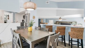 Une cuisine moderne avec un coin repas, comprenant une table en bois, des chaises en osier et un luminaire suspendu.