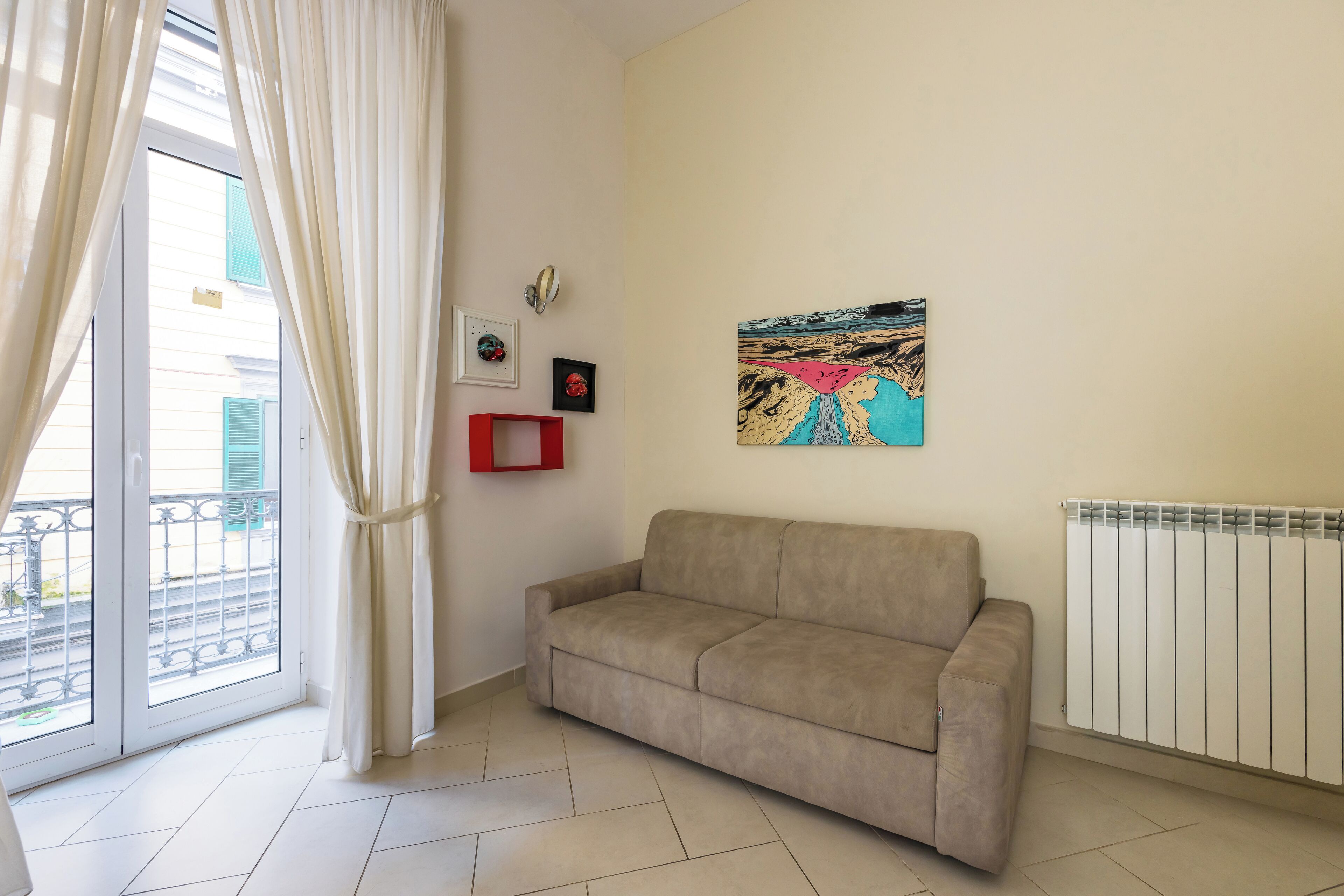 A living room with a beige sofa, a radiator, and a large window with curtains.