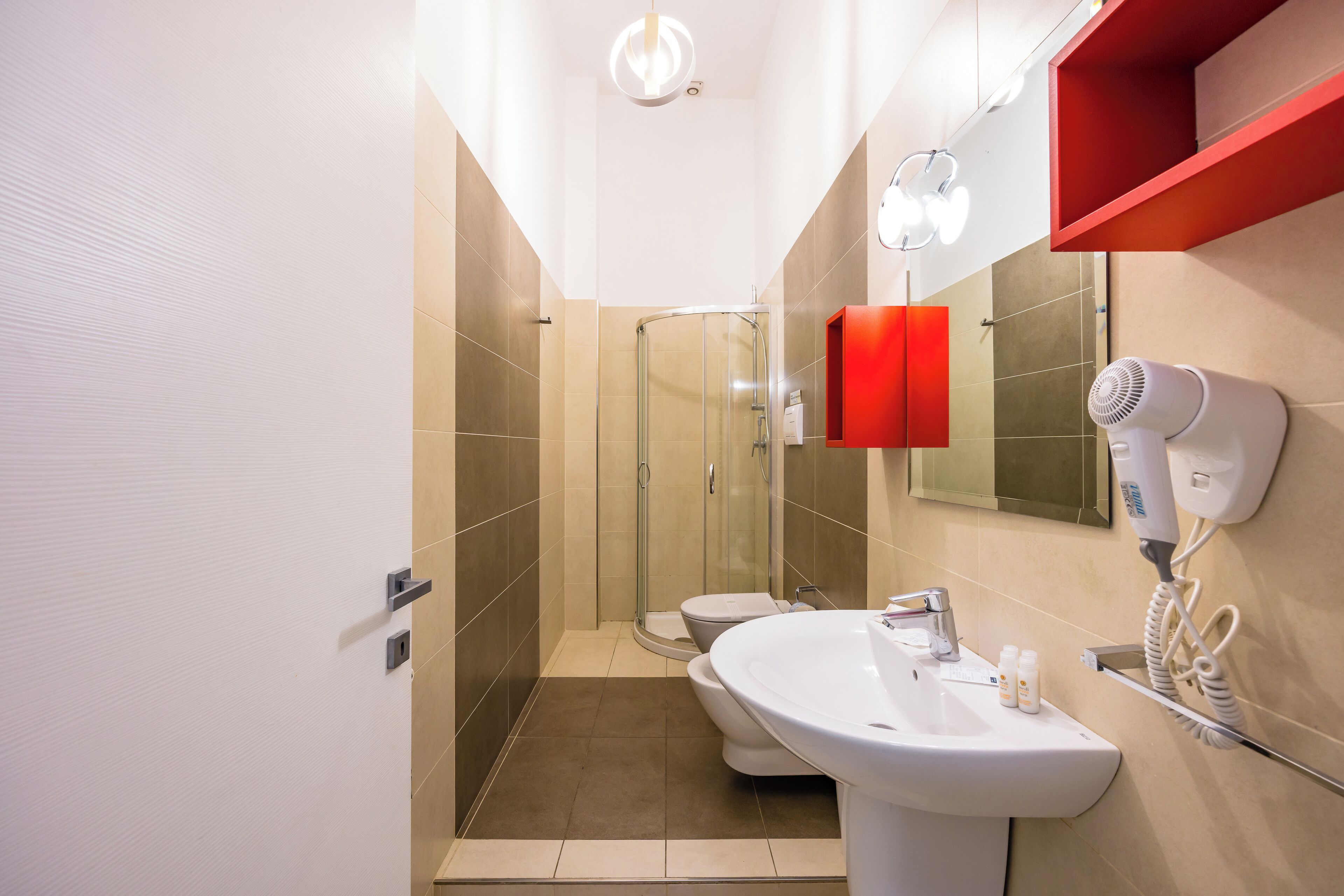 A modern bathroom with a glass shower enclosure, a white sink, and a hairdryer mounted on the wall.