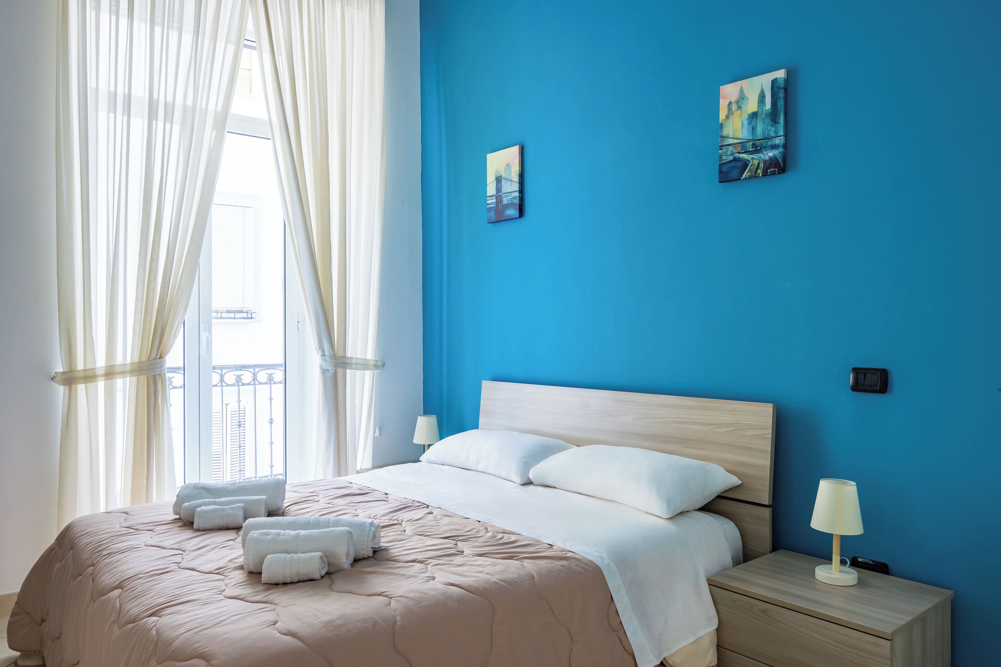 Une chambre à coucher avec un lit, des oreillers blancs, une table de chevet avec une lampe et deux tableaux accrochés au mur.