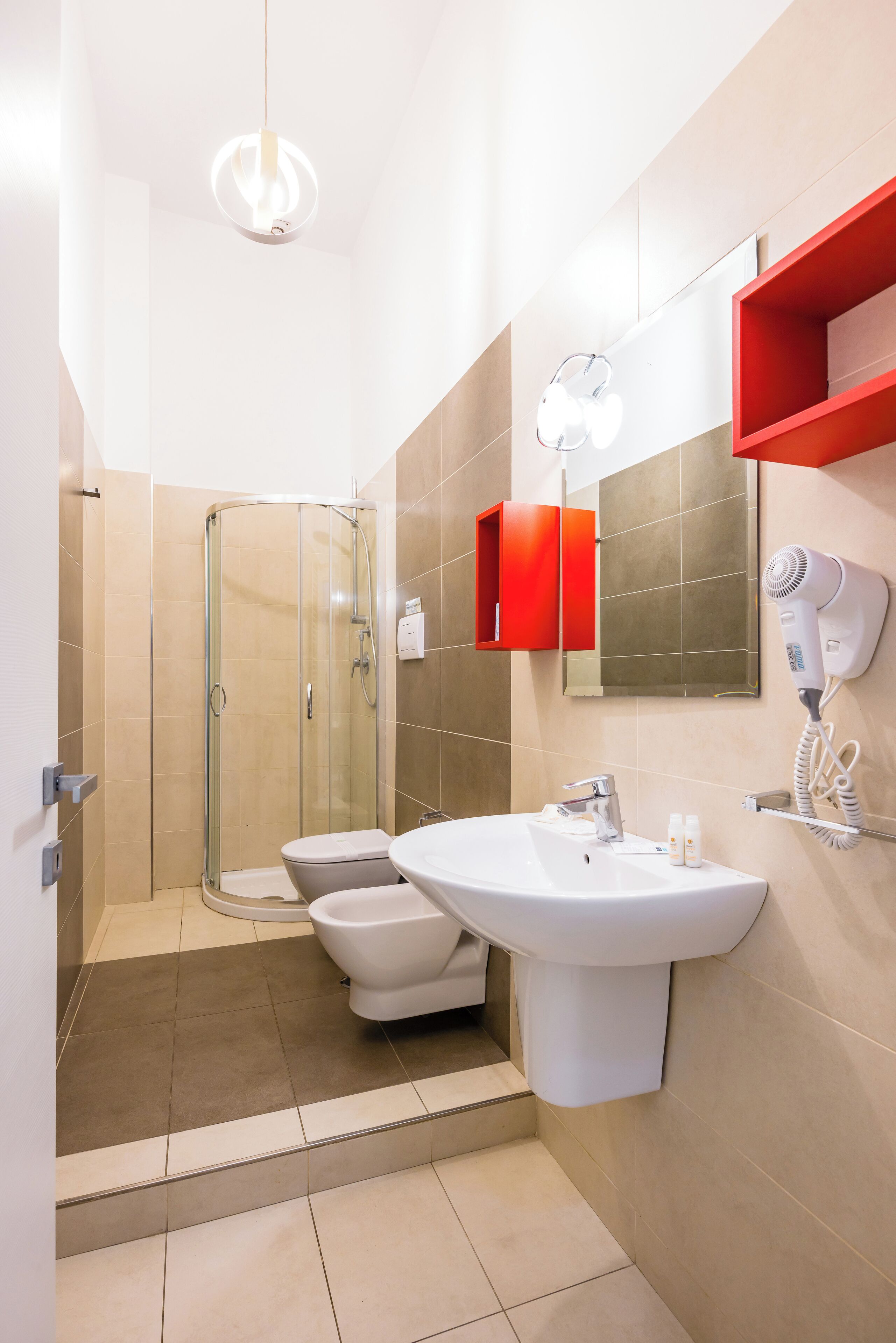 Et moderne badeværelse med bruseniche i glas, toilet, håndvask og en hårføner, der er monteret på væggen.