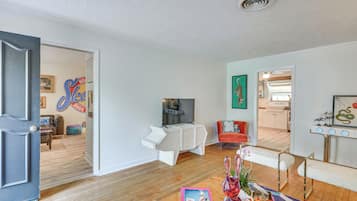 Una sala de estar moderna con un sofá, una mesa de centro y un televisor. Se observa una cocina al fondo.
