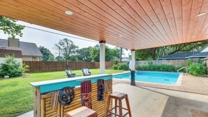 Un patio al aire libre con una barra de madera, dos taburetes y una piscina al fondo.