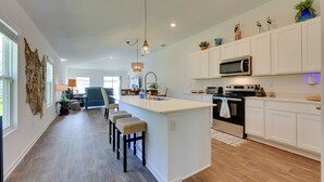 A modern kitchen with white cabinetry, a central island with bar stools, and a microwave. - Home Near Flagler Beach, Daytona, Parks & More! (Palm Coast)