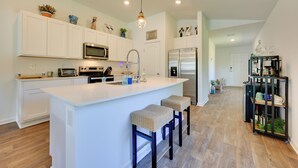 A modern kitchen with white cabinetry, a central island with bar stools, stainless steel appliances, and a pendant light. - Home Near Flagler Beach, Daytona, Parks & More! (Palm Coast)