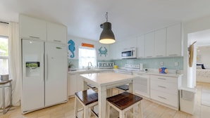 A modern kitchen with white cabinets, a central island with stools, a refrigerator, microwave, and a hanging pendant light. - Lanai, Pool & Patios: Waterfront Home in Tavernier (Tavernier)