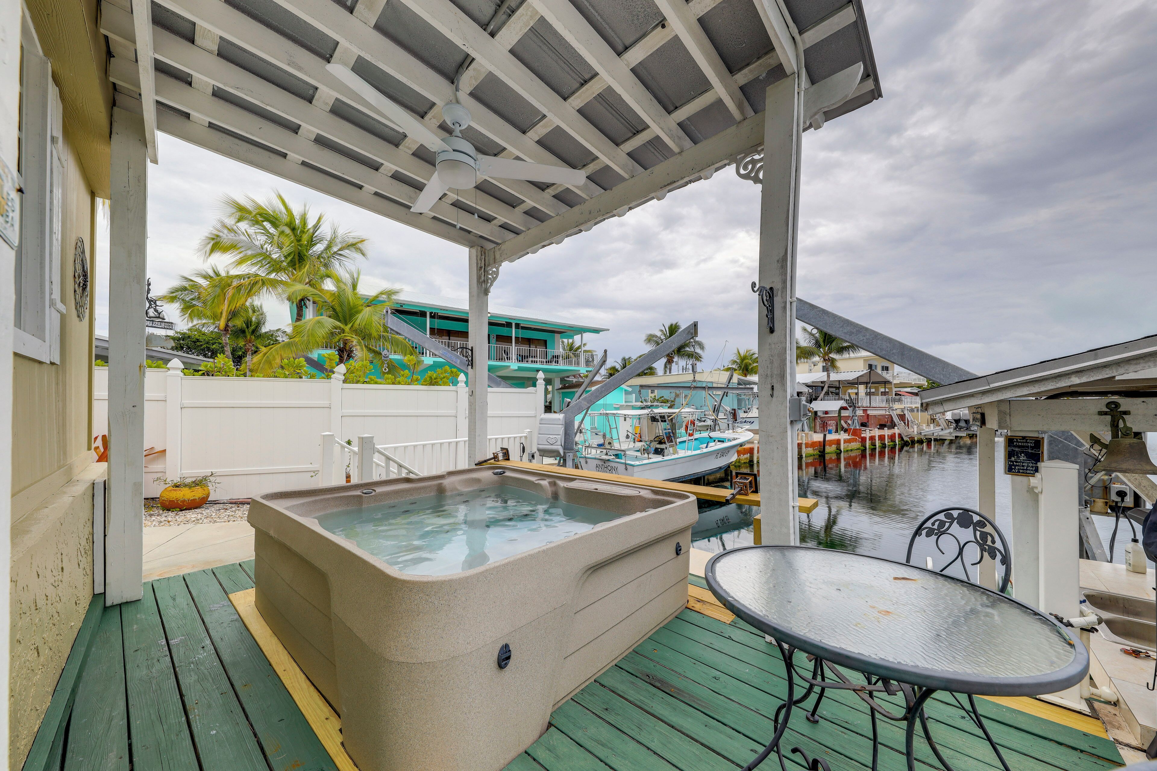 A hot tub on a wooden deck with a covered patio, overlooking a marina with boats.