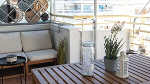 A wooden table and a cushioned bench under a shaded area with a view of buildings.