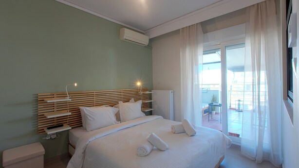 A modern hotel room with a large bed, a bedside table, a built-in shelf, and a view of the outdoor area.