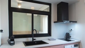 A compact kitchen with a sink, a coffee maker, a washing machine, and a window with a view of the outside.