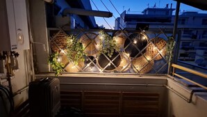 A window with woven baskets and plants, a suitcase, and a view of buildings at dusk.