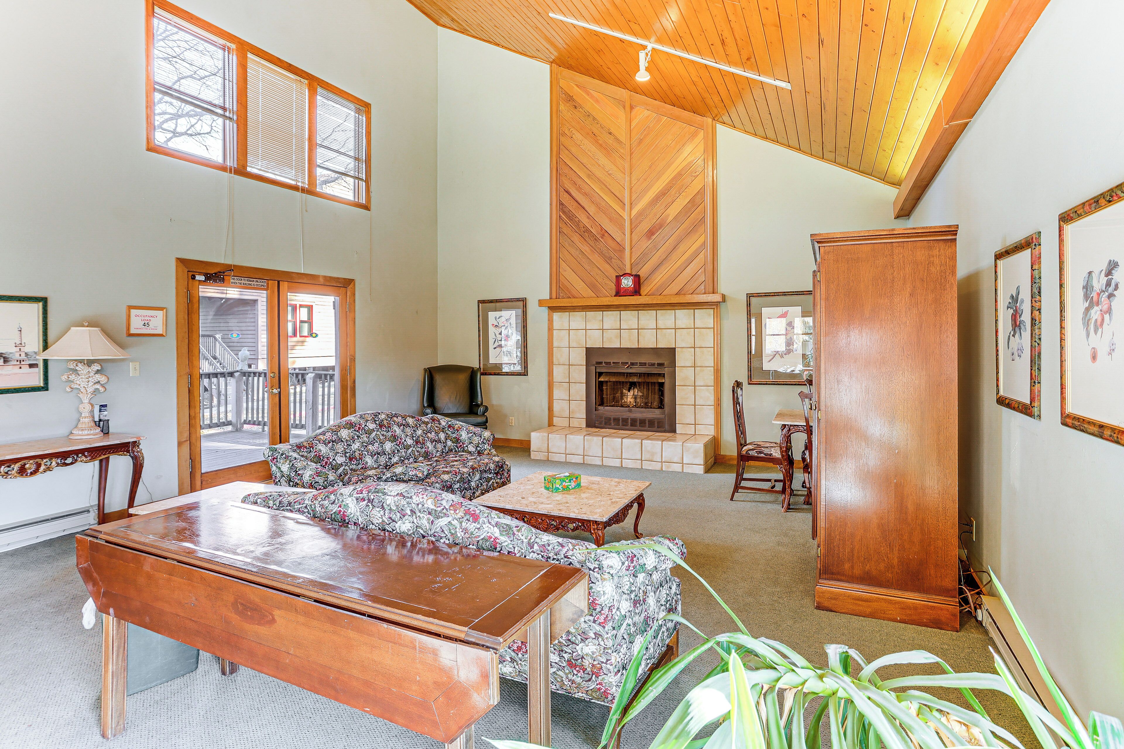 A spacious living room with a fireplace, wooden ceiling, and large windows.