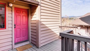 Una casa con puerta roja, terraza de madera y vistas del paisaje circundante.