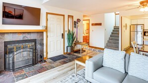 Una sala de estar con chimenea, un sofá y una escalera que lleva a una cocina.
