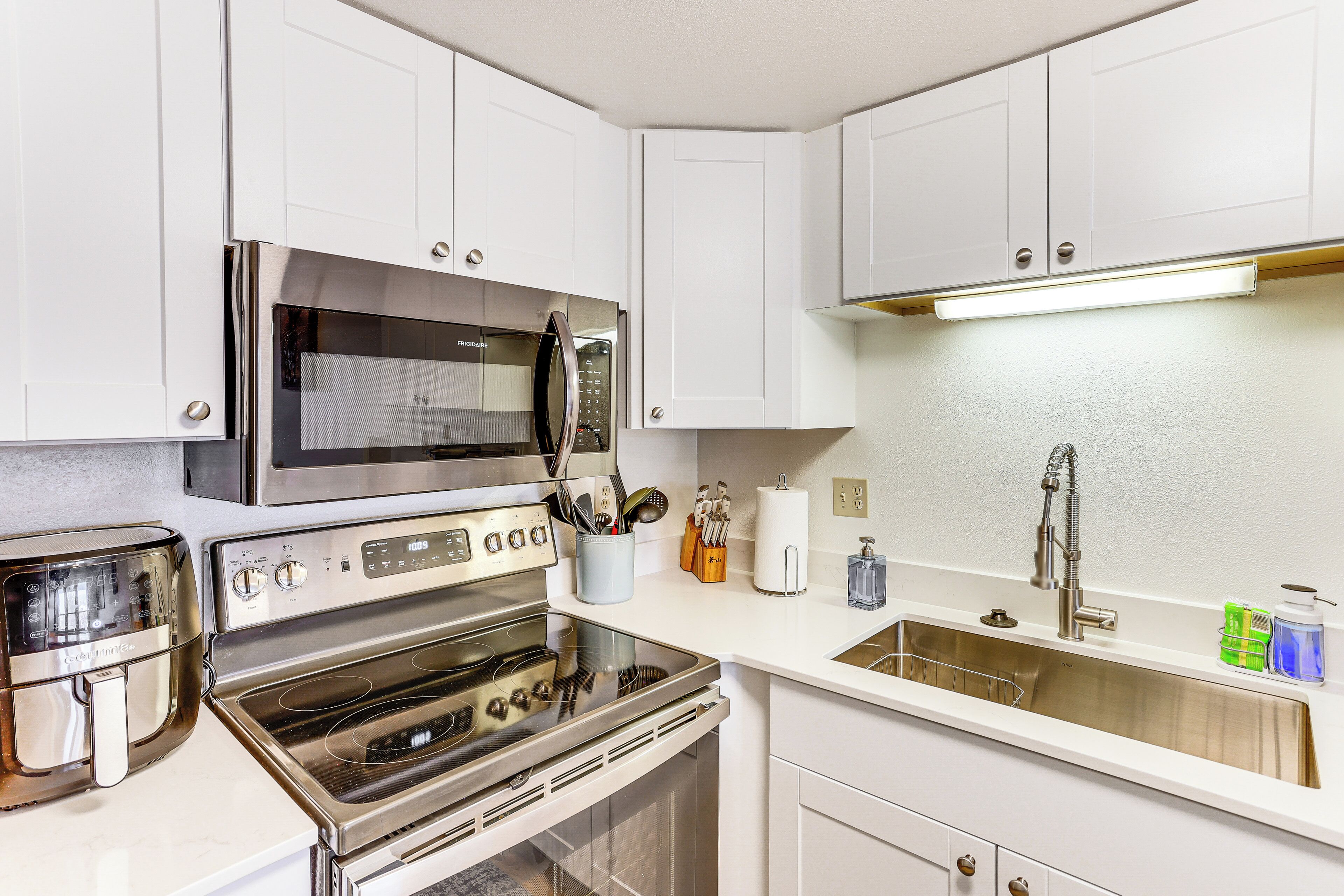 A modern kitchen with white cabinets, stainless steel appliances, a microwave, an oven, and a sink.